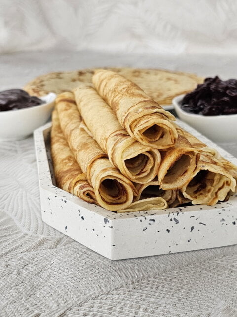 Thin golden crepes stacked with fresh fruit toppings and a drizzle of chocolate.