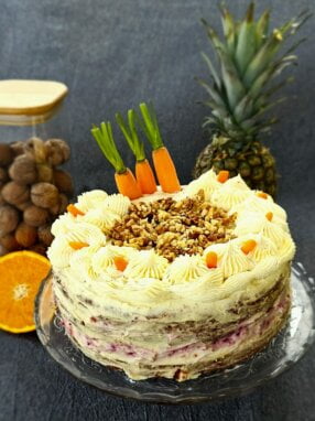 Moist Carrot Cake with cream cheese frosting and raspberry jam garnished with fresh carrots and nuts