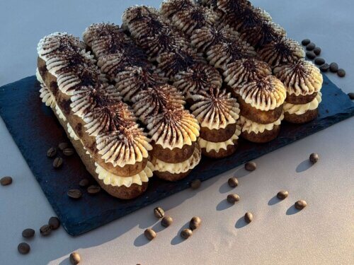 Tiramisu dessert with layers of coffee-soaked ladyfingers, mascarpone, and cocoa, served on a white plate.
